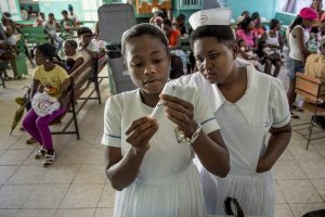 Medicinska sestra na Haitiju pogleda študentki zdravstvene nege čez ramo in preveri, ali pravilno polni iglo. Foto: USAID Ameriška agencija za mednarodni razvoj CCBY